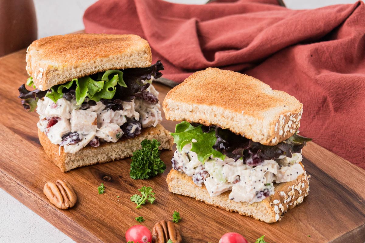 A turkey salad sandwich cut in half and placed on a wood board.