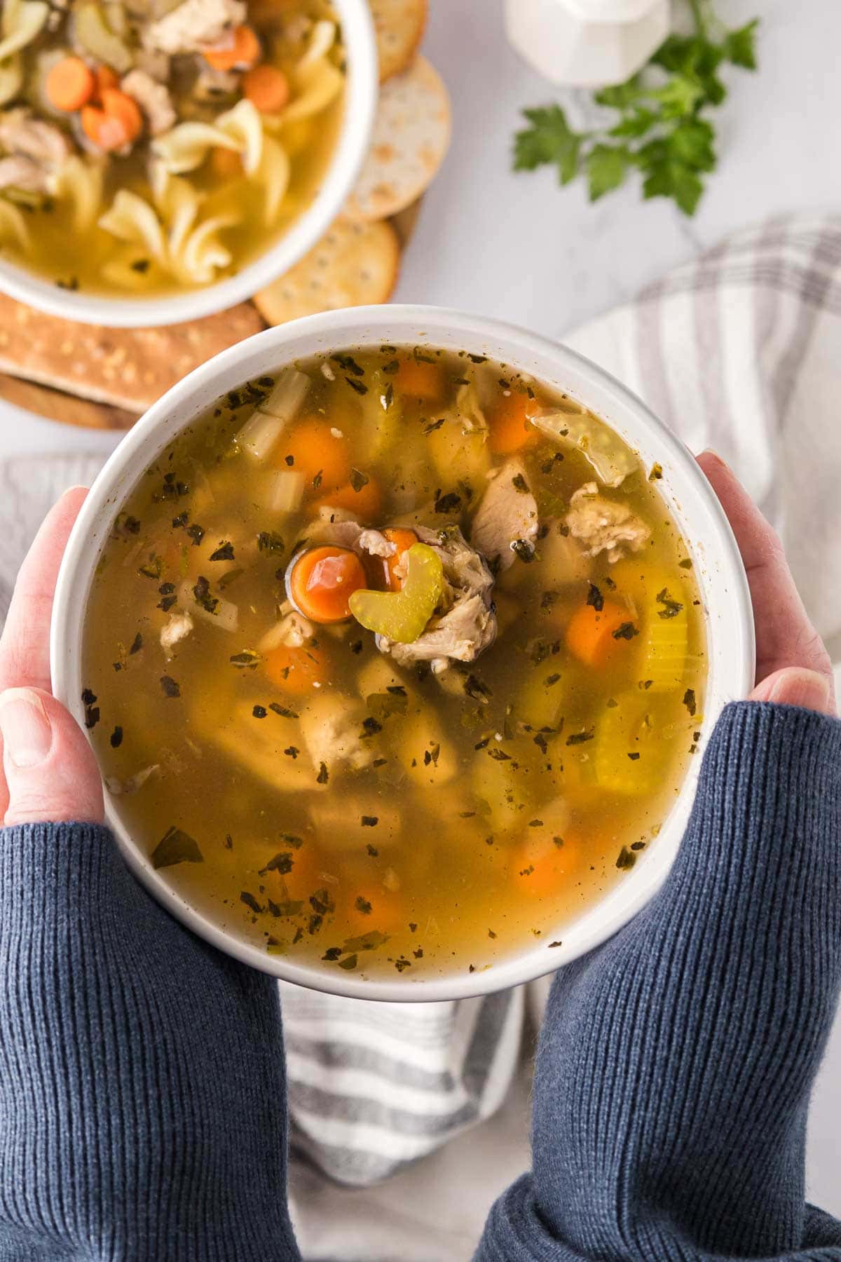 Two hands picking up a bowl of soup to set it on the table.