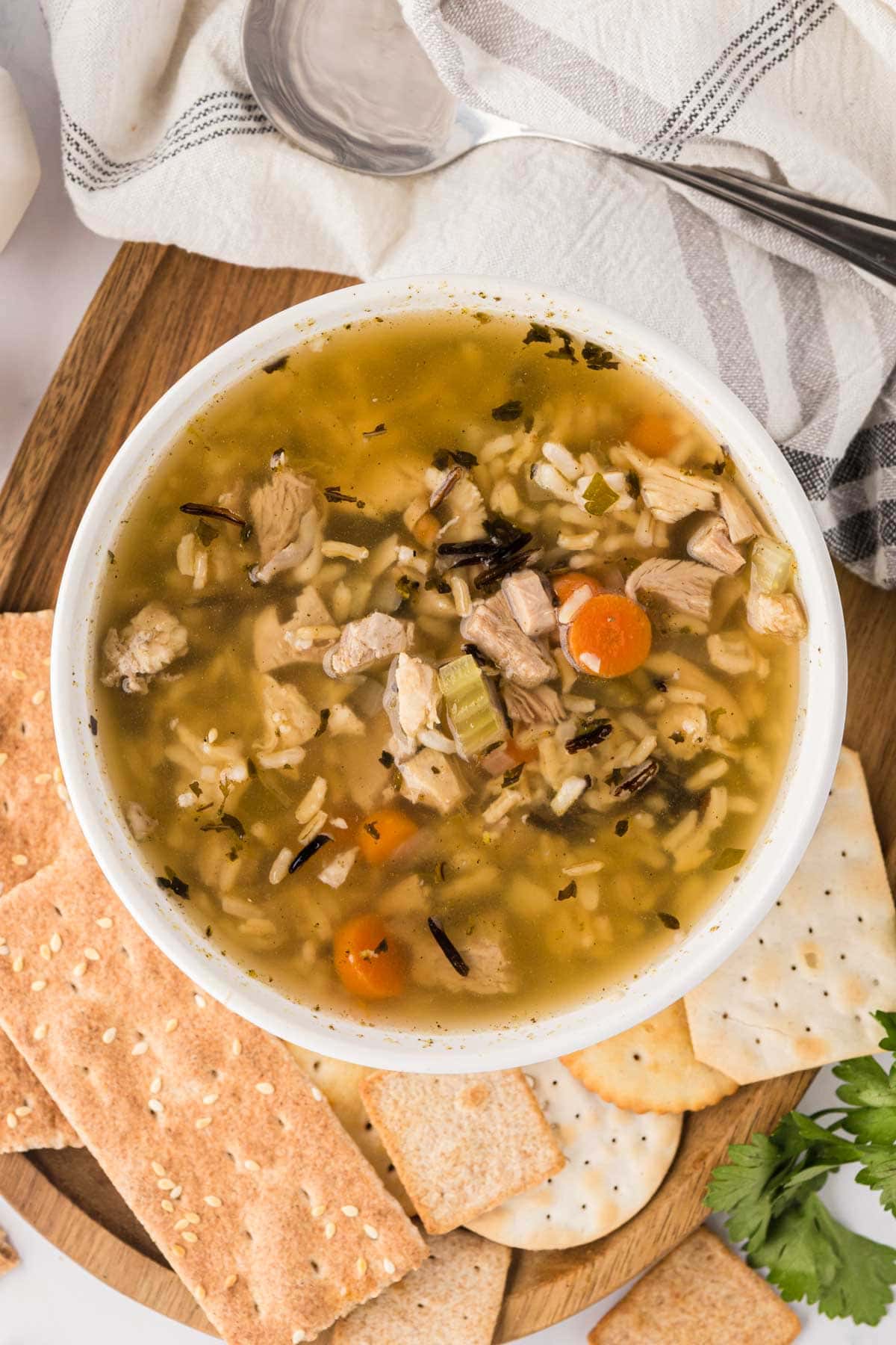 A bowl of turkey soup with rice on a wooden board served with crackers.