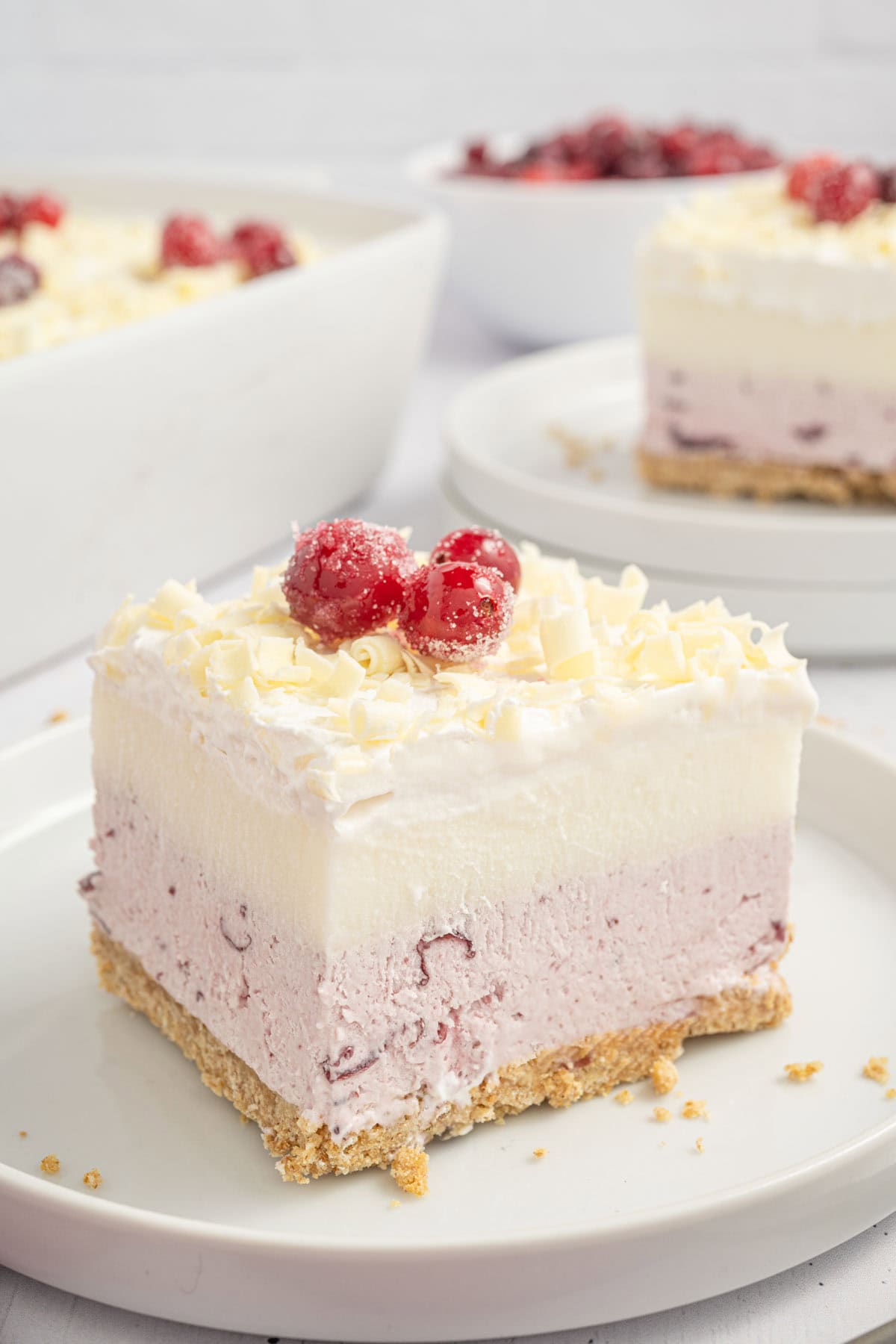 Slice of white chocolate cranberry dessert on a plate with another slice in the background.