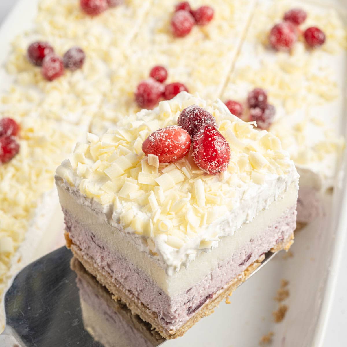 White chocolate cranberry dessert in a baking dish with a metal spatula taking one piece out.