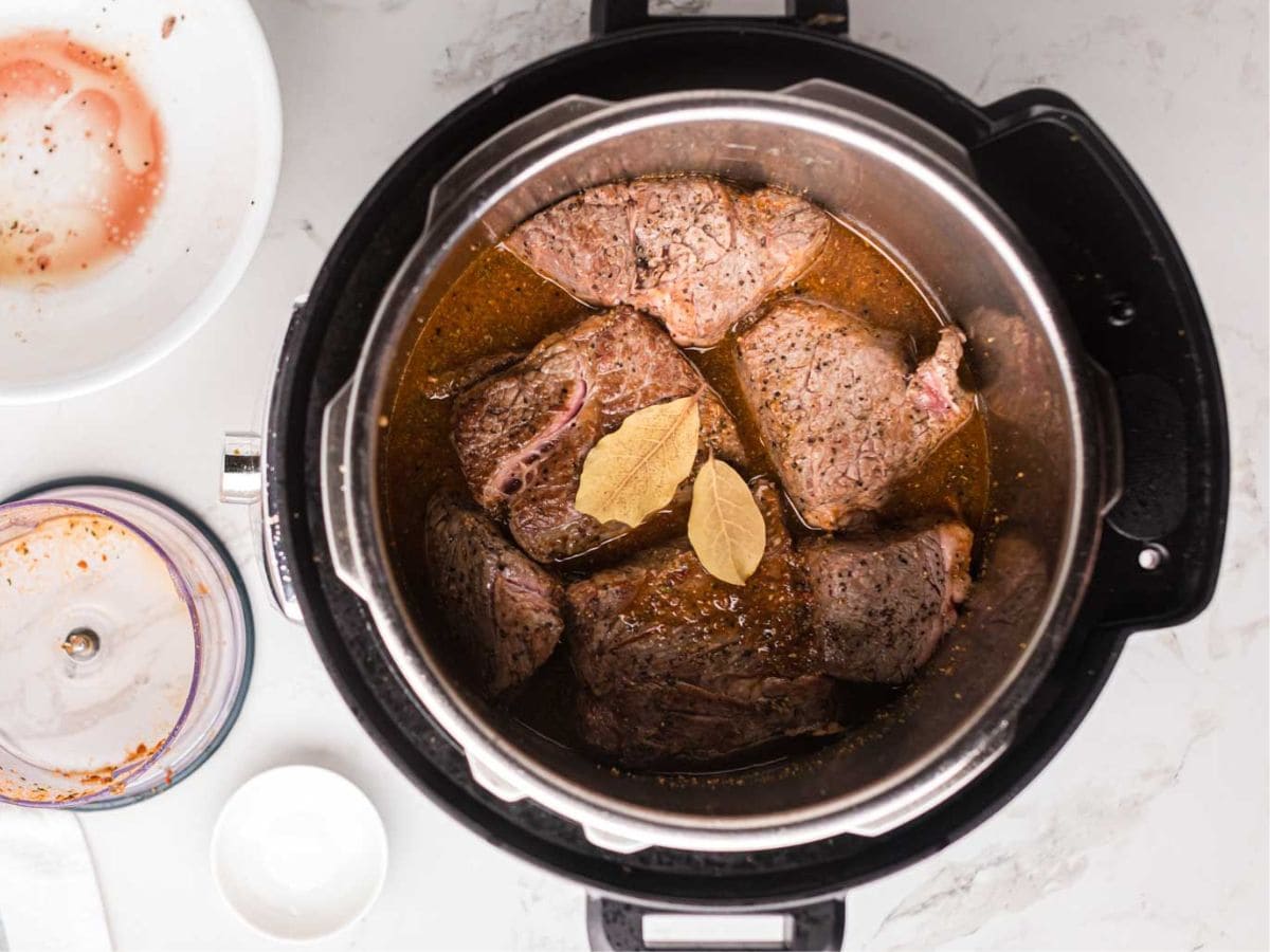 Chuck roast chunks added to the instant pot with two bay leaves.