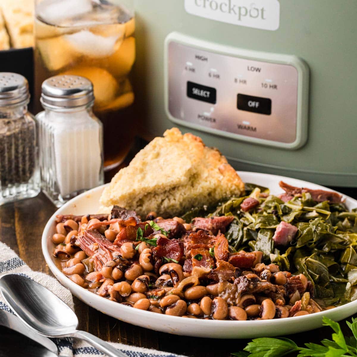 A white plate with Black Eyed Peas, collard greens and cornbread.