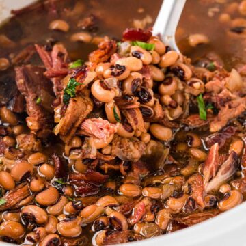 A spoon removing a scoop of black eyed peas from a slow cooker.