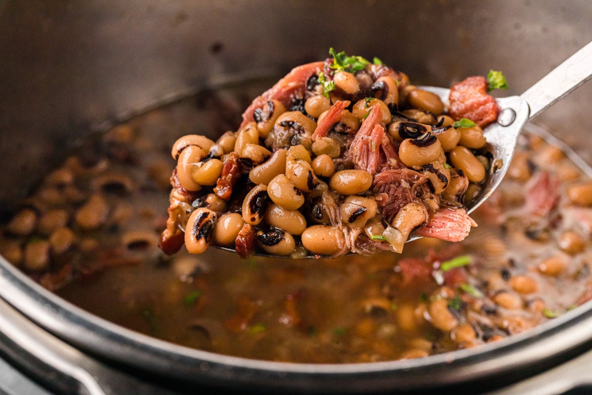 A large serving spoon, removing a scoop of Black Eyed Peas with shredded pieces of ham and bacon.