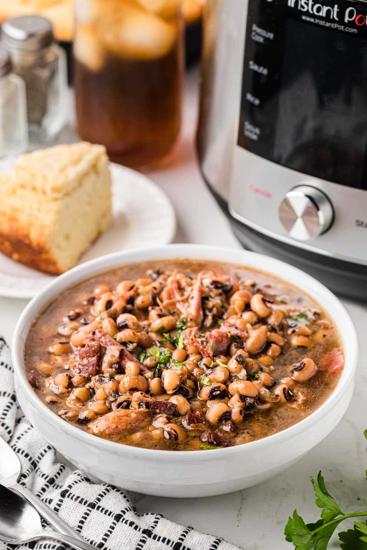 A white serving bowl of southern Black Eyed Peas with an instant pot in the background.