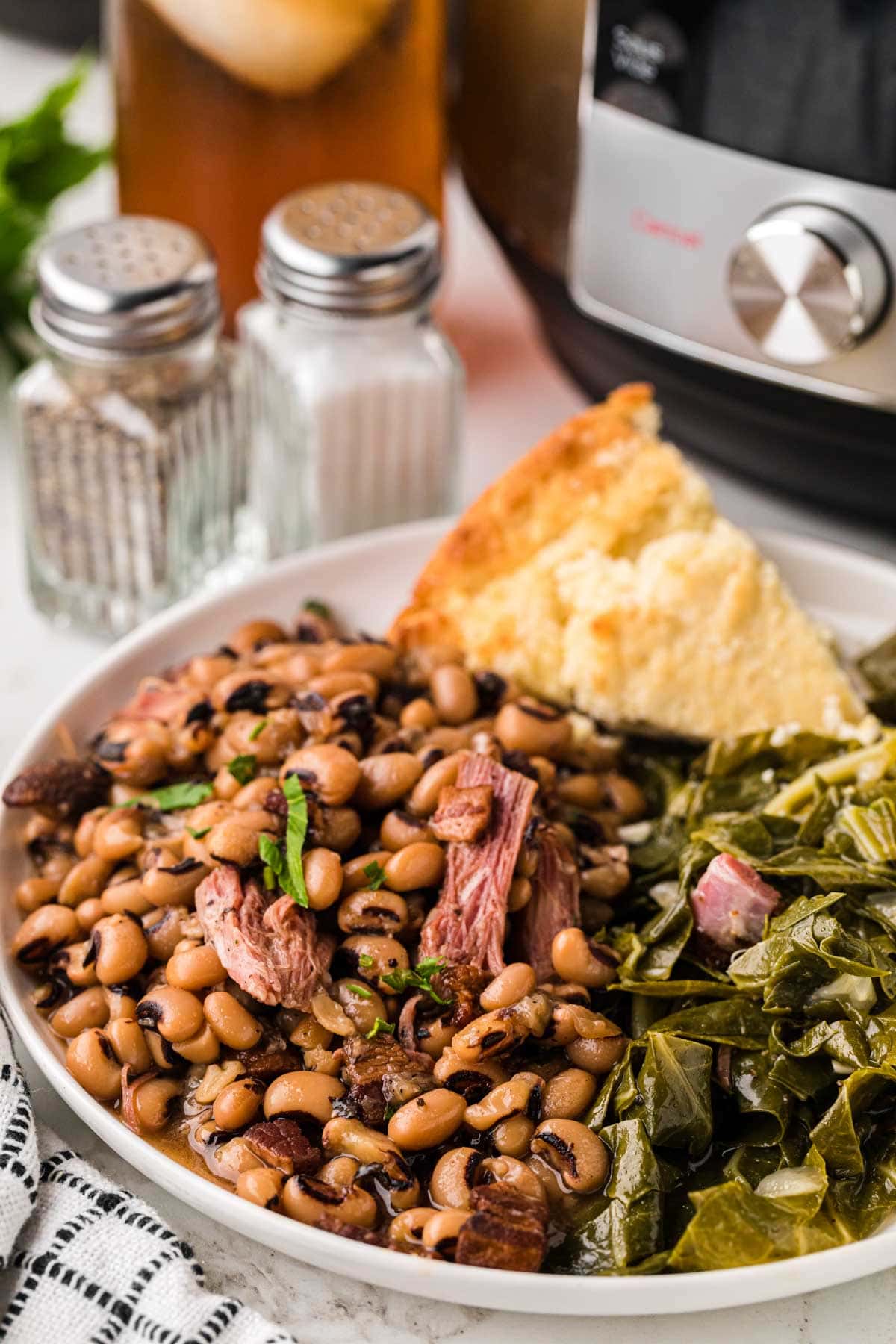 A white plate with Black Eyed Peas, collard greens and cornbread.