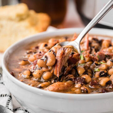 A spoon removing a serving of southern Black Eyed Peas from a white bowl with an instant pot in the background.