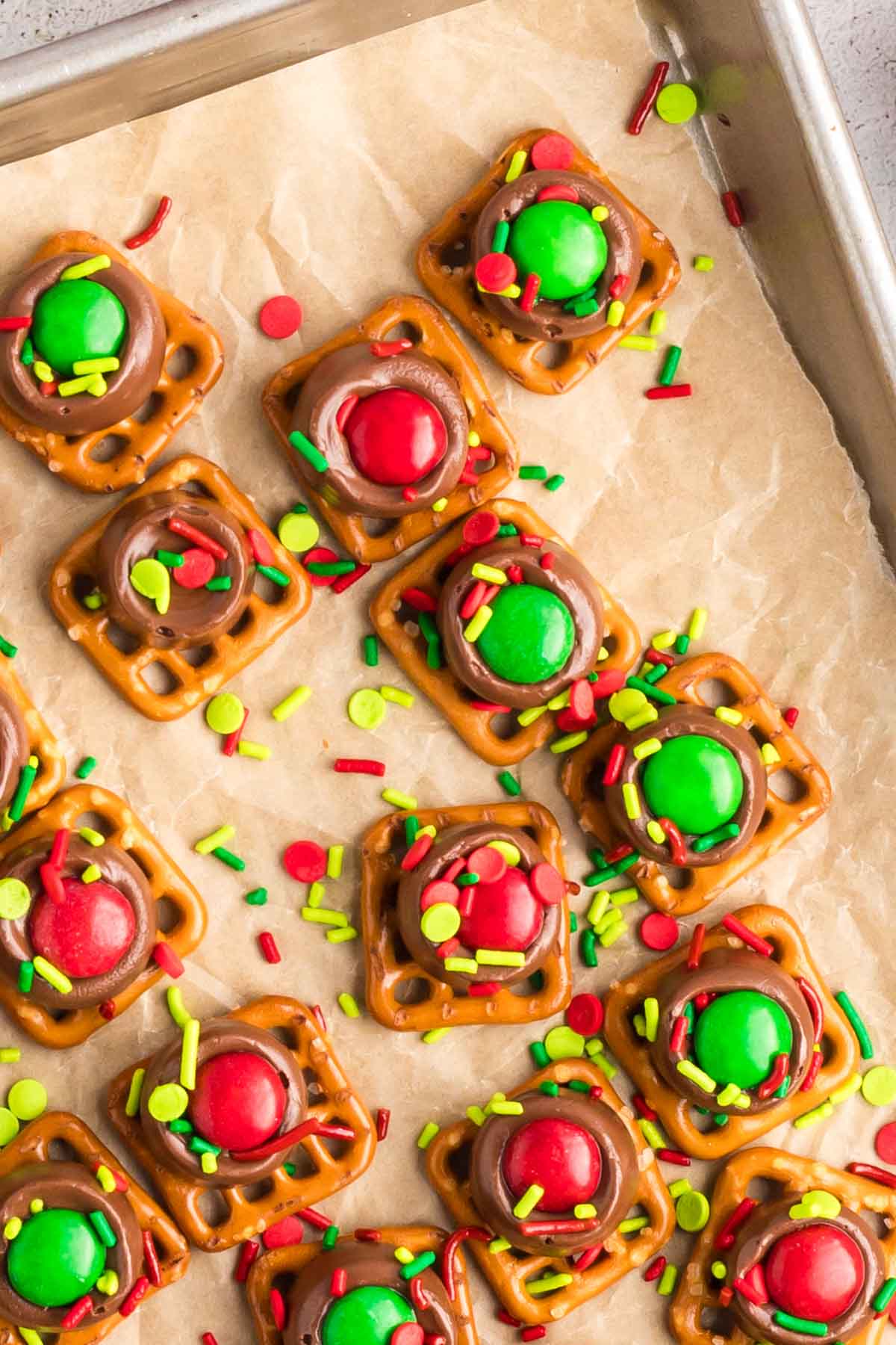 Red and green M&Ms and festive sprinkles on top of a Rolo slightly melted on a pretzel.