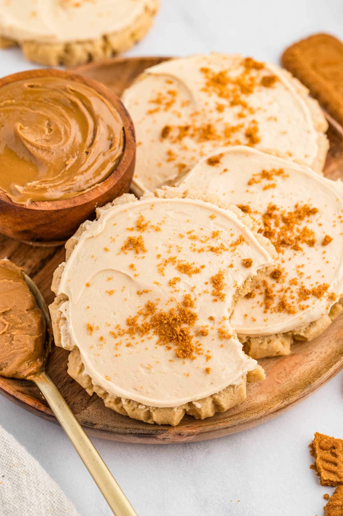 Plate of frosted cookie butter cookies with one missing a bite next to a ramekin of cookie butter.