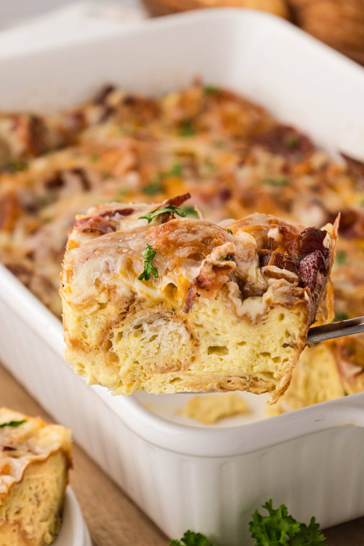 A slice of the savory croissant casserole being removed with a spatula from a white casserole dish.