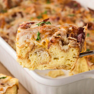 A slice of the savory croissant casserole being removed with a spatula from a white casserole dish.