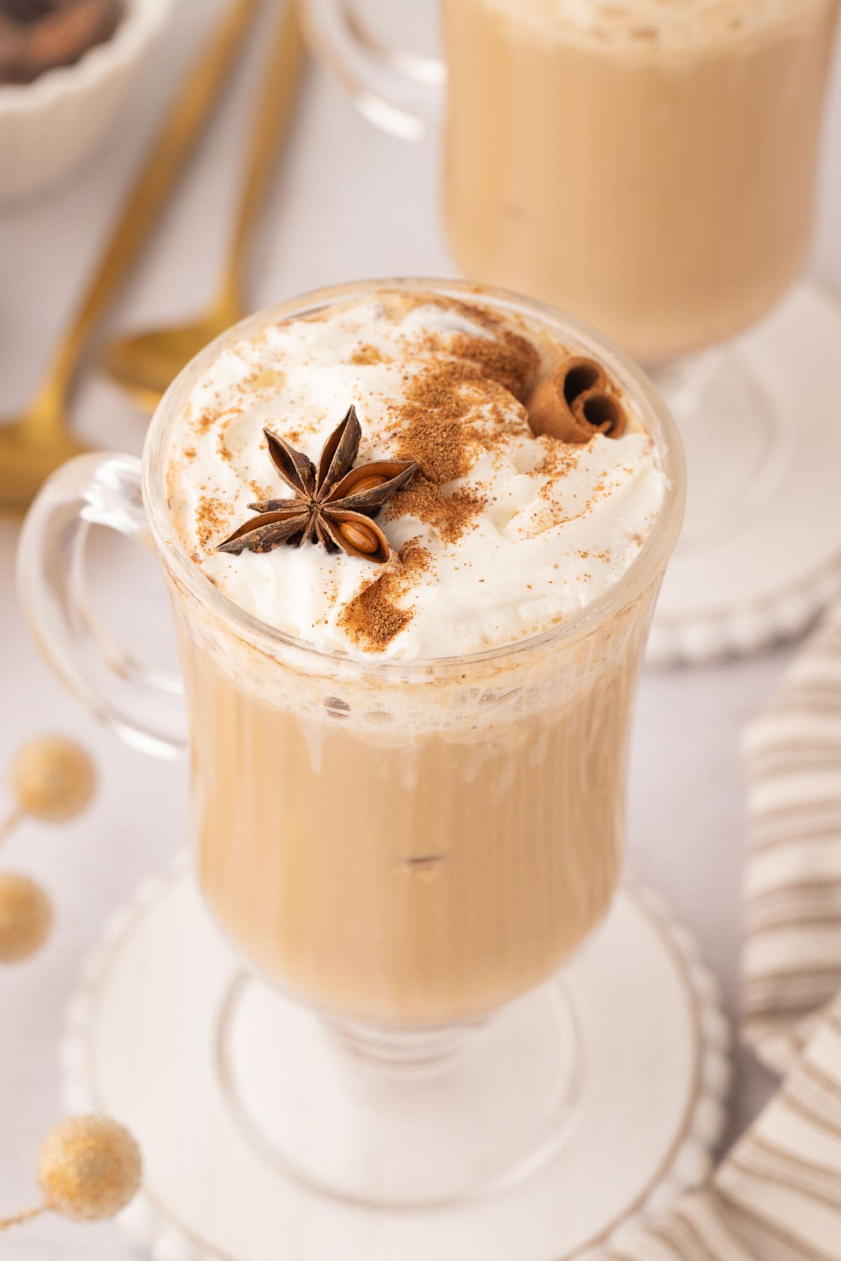 And up close in image of the glass mug with eggnog latte, top with whipped cream, cinnamon, cinnamon stick, and a star anise for garnish.