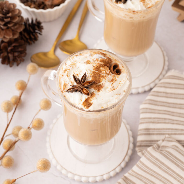 Two eggnog latte set on a white wooden coaster.