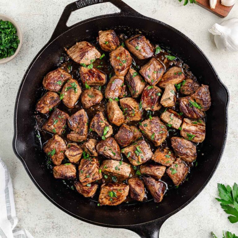 Garlic butter infused steak bites in a cast iron pan sprinkled with parsley.