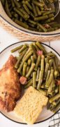 An overhead shot of Southern green beans with bacon is plated with cornbread and fried chicken.