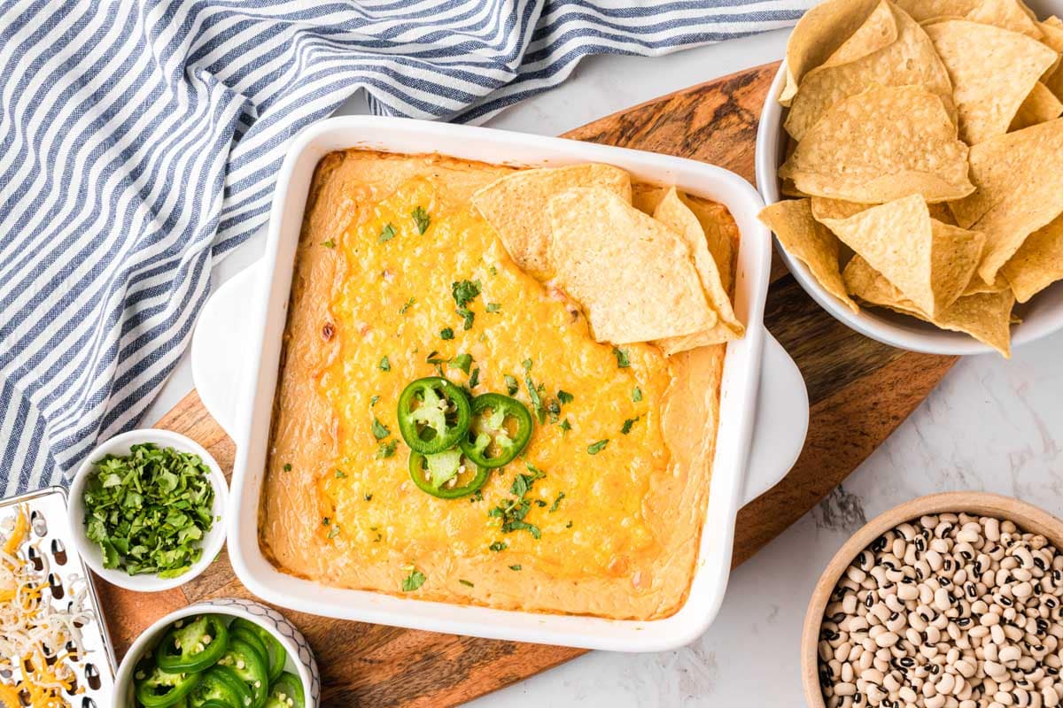 An overhead image of a baking dish filled with black-eyed peas dip, garnished with sliced jalapeños, cilantro, and tortilla chips served on a wooden serving board.