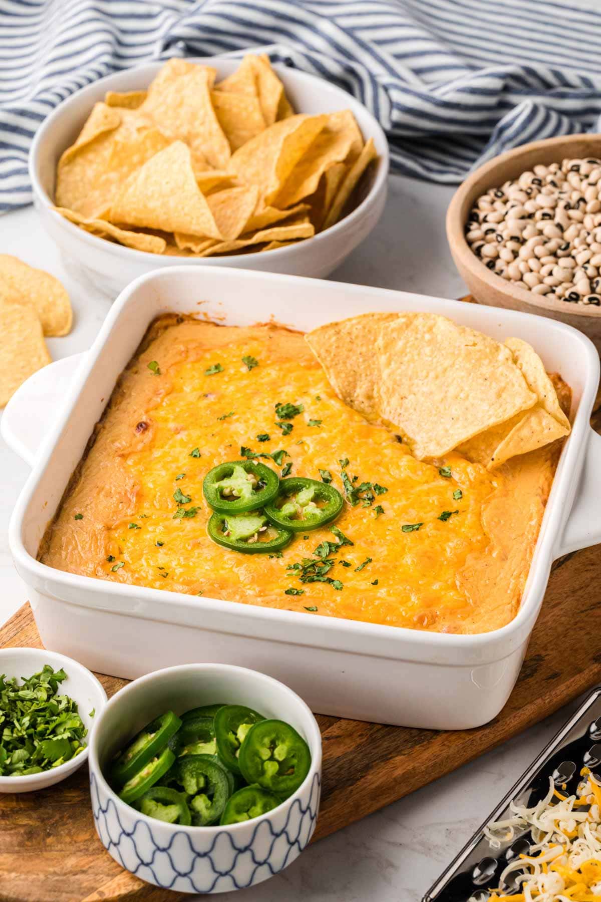 A baking dish filled with black dip, served warm from the oven with garnishes of jalapeños, cilantro and tortilla chips.