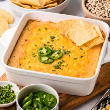 A baking dish filled with black dip, served warm from the oven with garnishes of jalapeños, cilantro and tortilla chips.