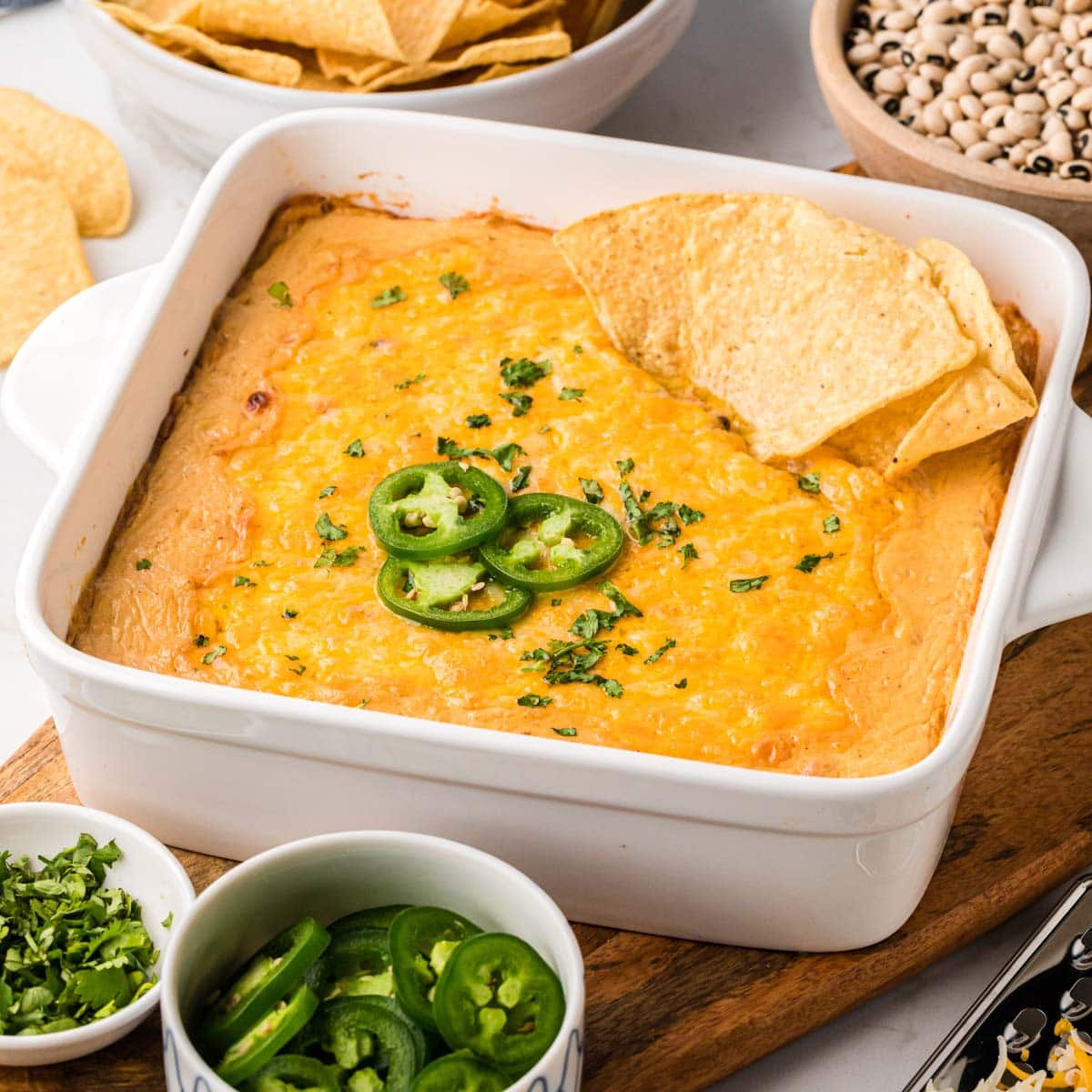 A baking dish filled with black dip, served warm from the oven with garnishes of jalapeños, cilantro and tortilla chips.