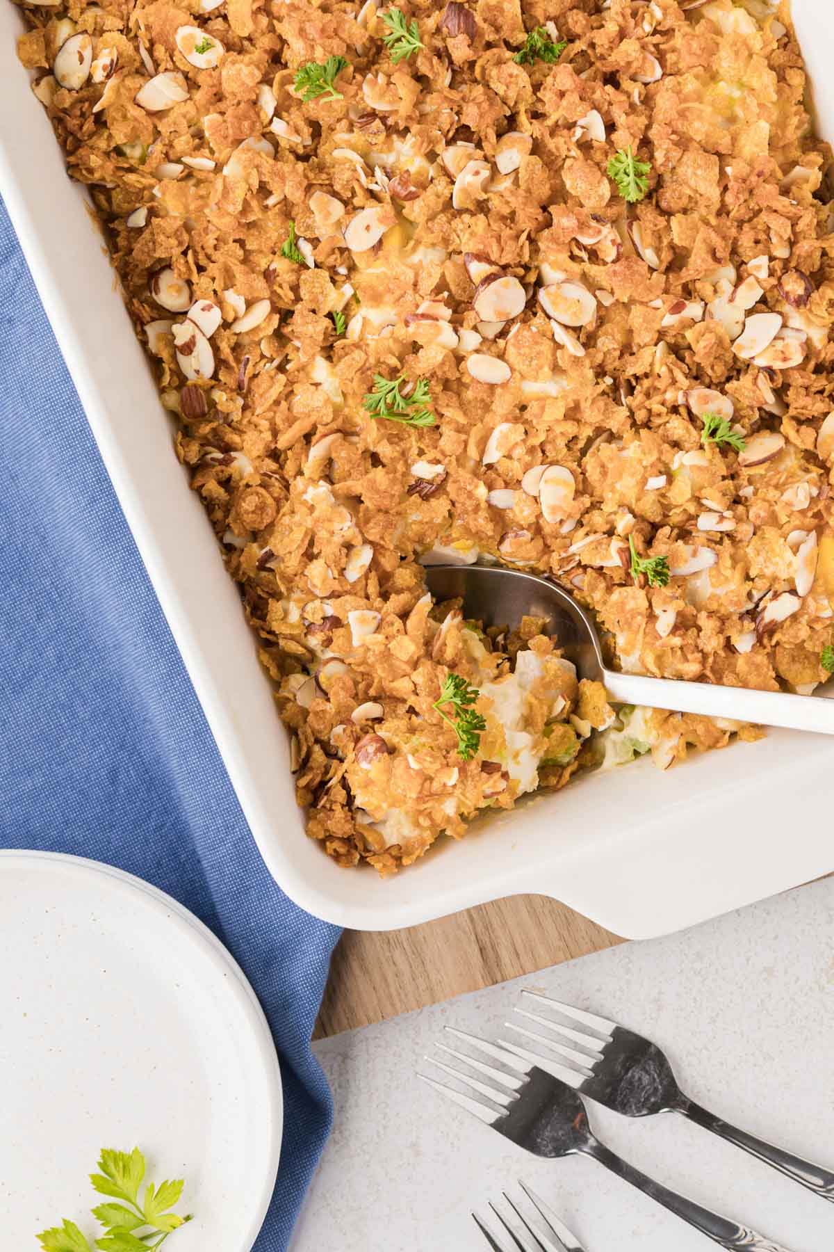 A white casserole dish filled with hot chicken casserole with a silver serving spoon removing a scoop.