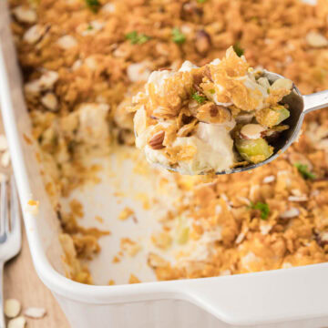 A white casserole dish filled with hot chicken casserole with a silver serving spoon removing a scoop.