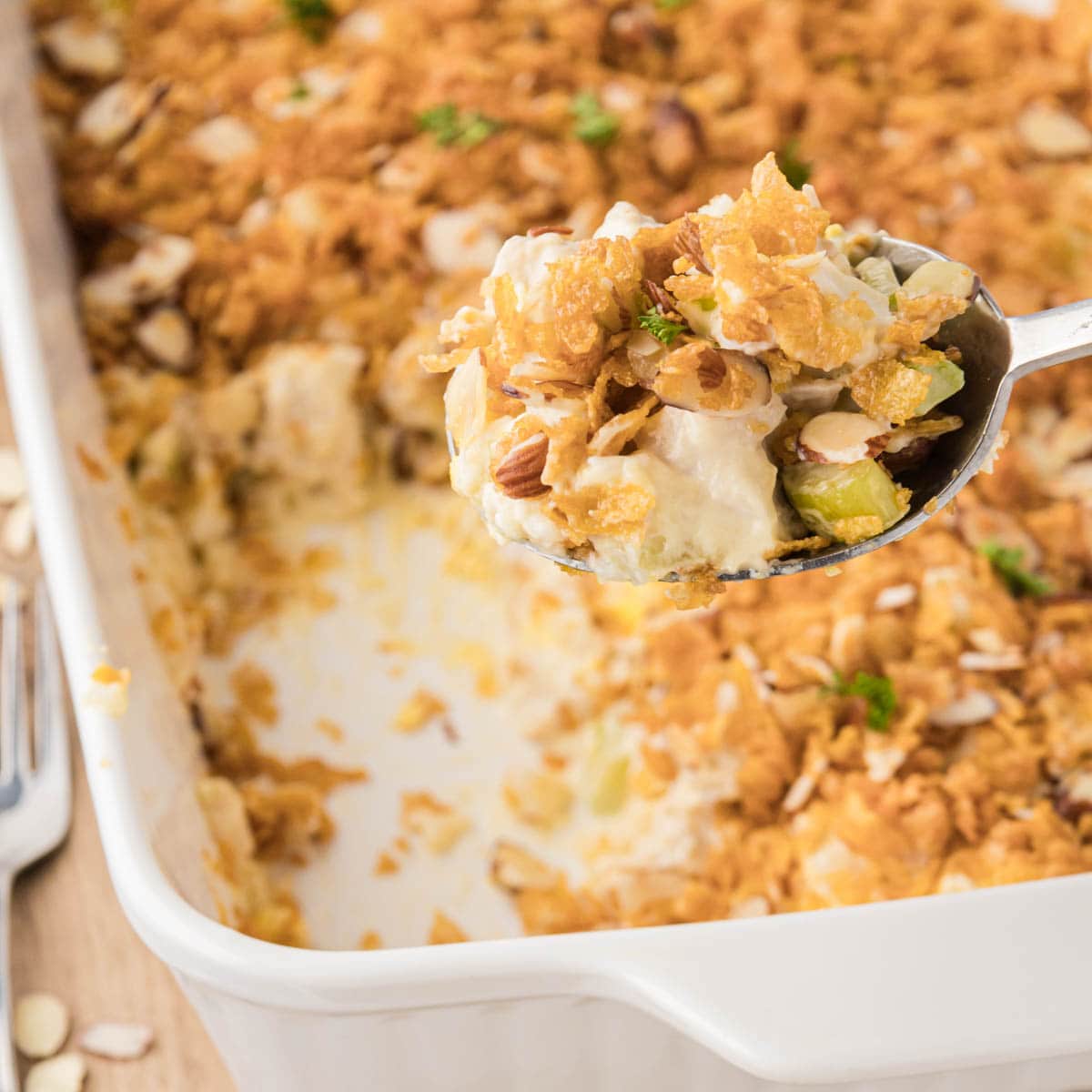 A white casserole dish filled with hot chicken casserole with a silver serving spoon removing a scoop.