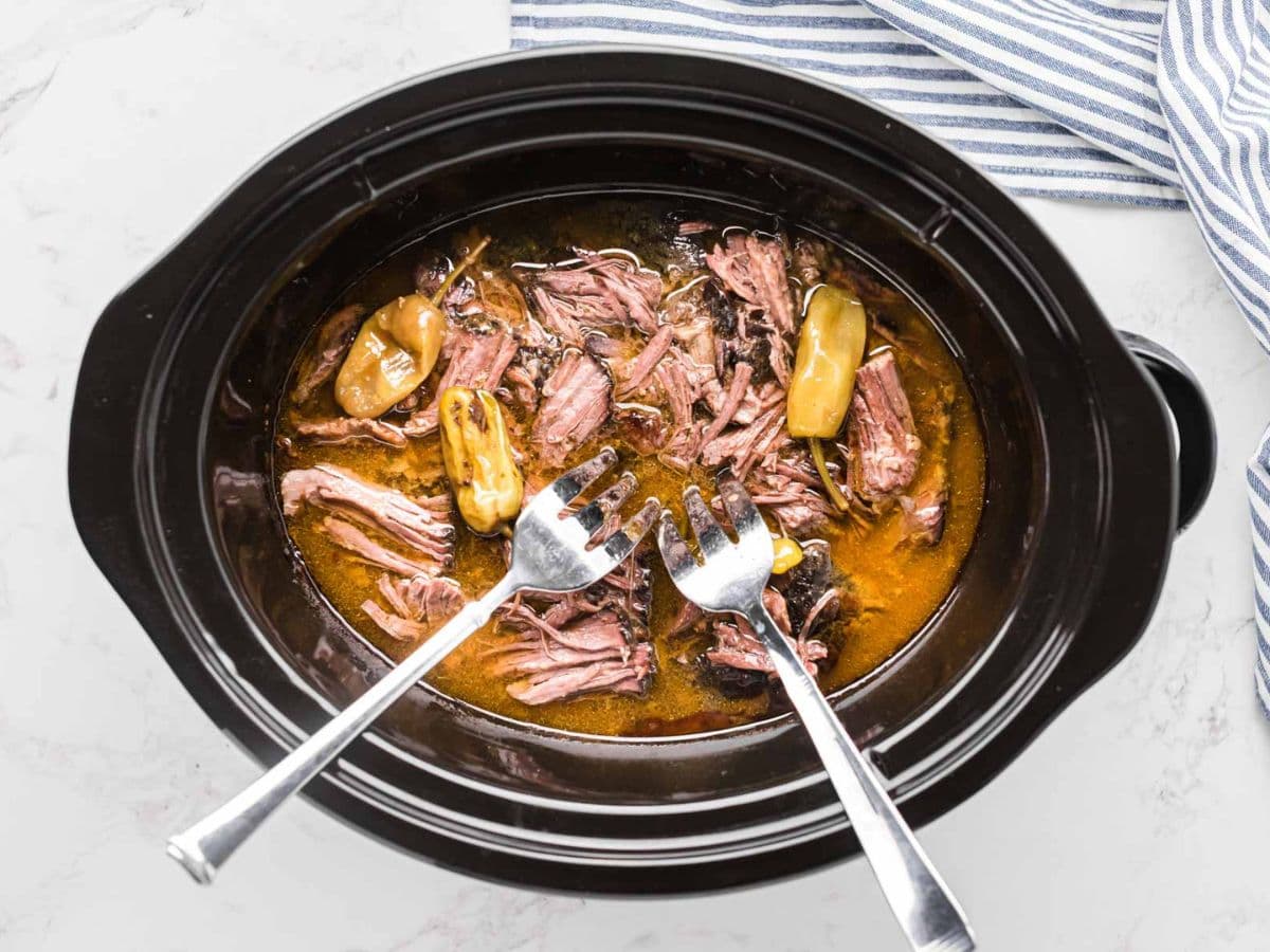 Two forks shredding the roast in the slow cooker.