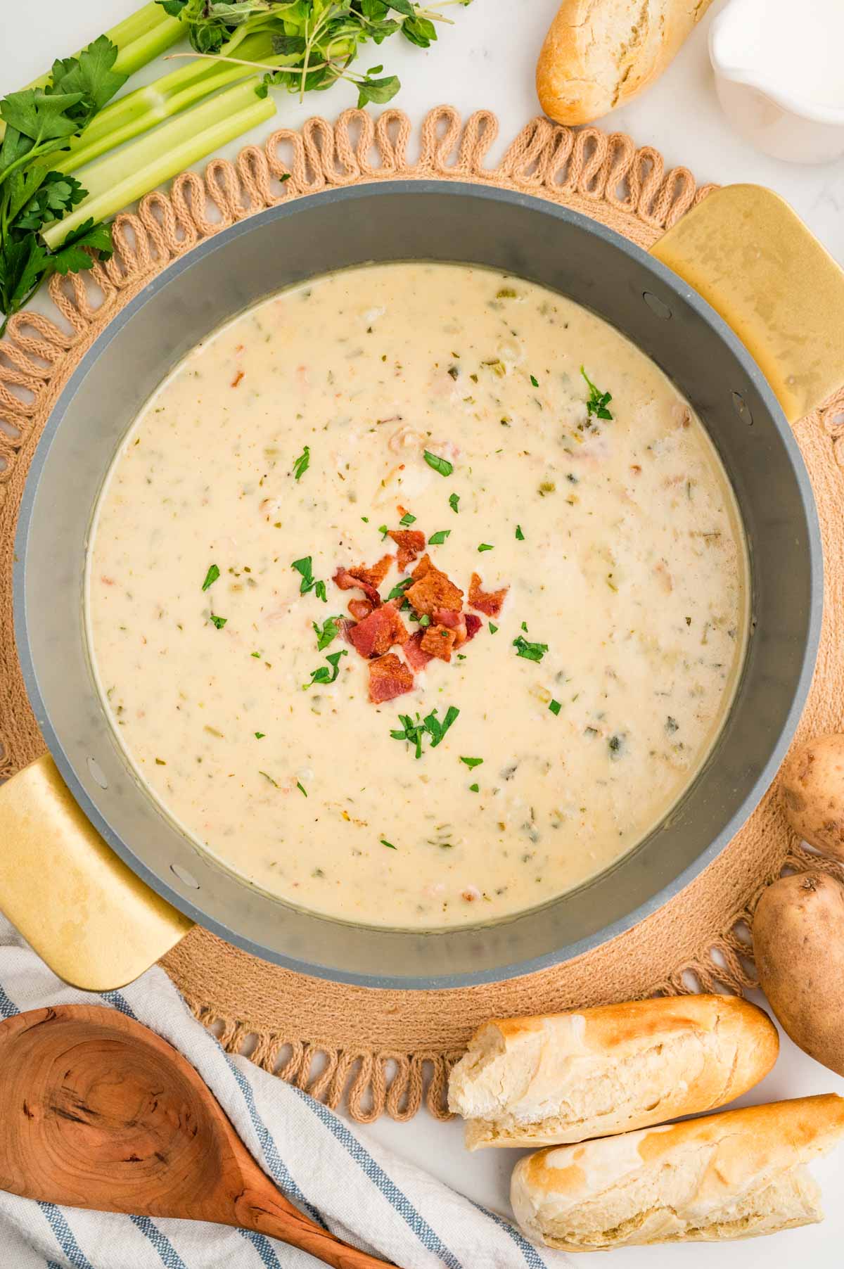 Overhead shot of clam chowder in a large stock pot surrounded by bread, potatoes and celery.