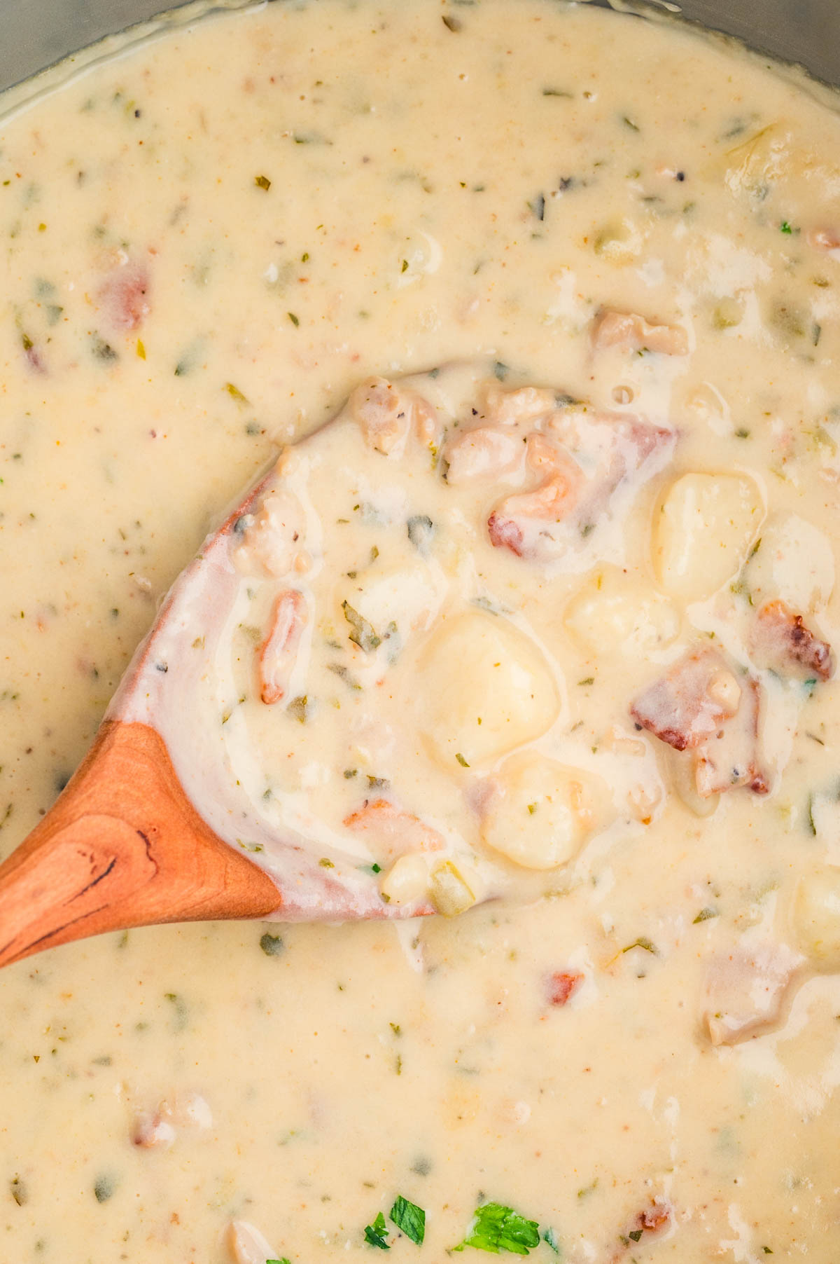 Clam chowder in a pot with a wooden spoon stirring the soup.