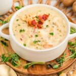 Close shot of clam chowder in a soup bowl topped with oyster crackers and chopped bacon.