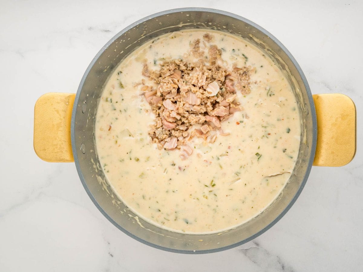 Adding the clams to the clam chowder in a large pot.