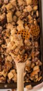 From overhead, this image is of the Praline Snack Mix on the baking sheet with a wooden spoon filled to show the ingredients.