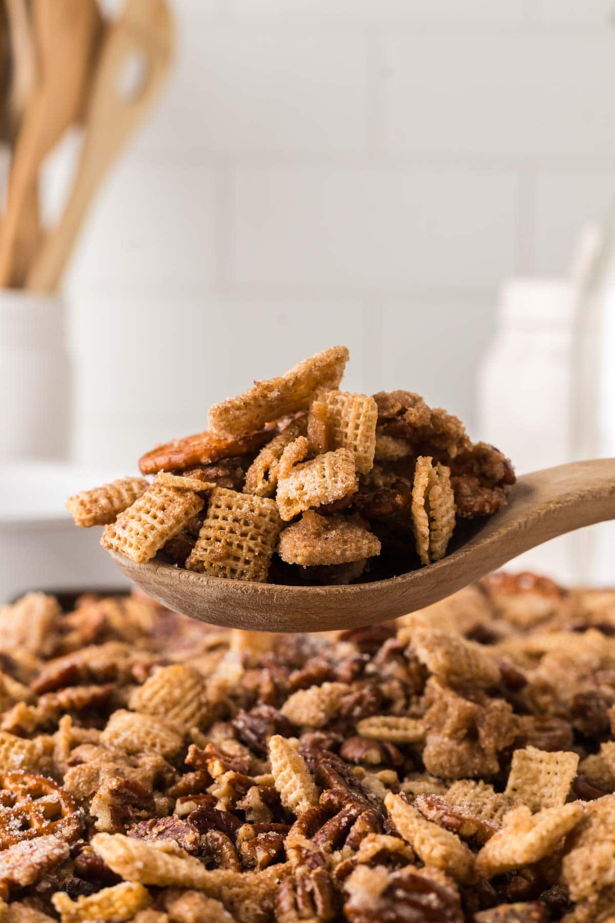 Wooden spoon scooping up praline snack mix from the sheet pan.