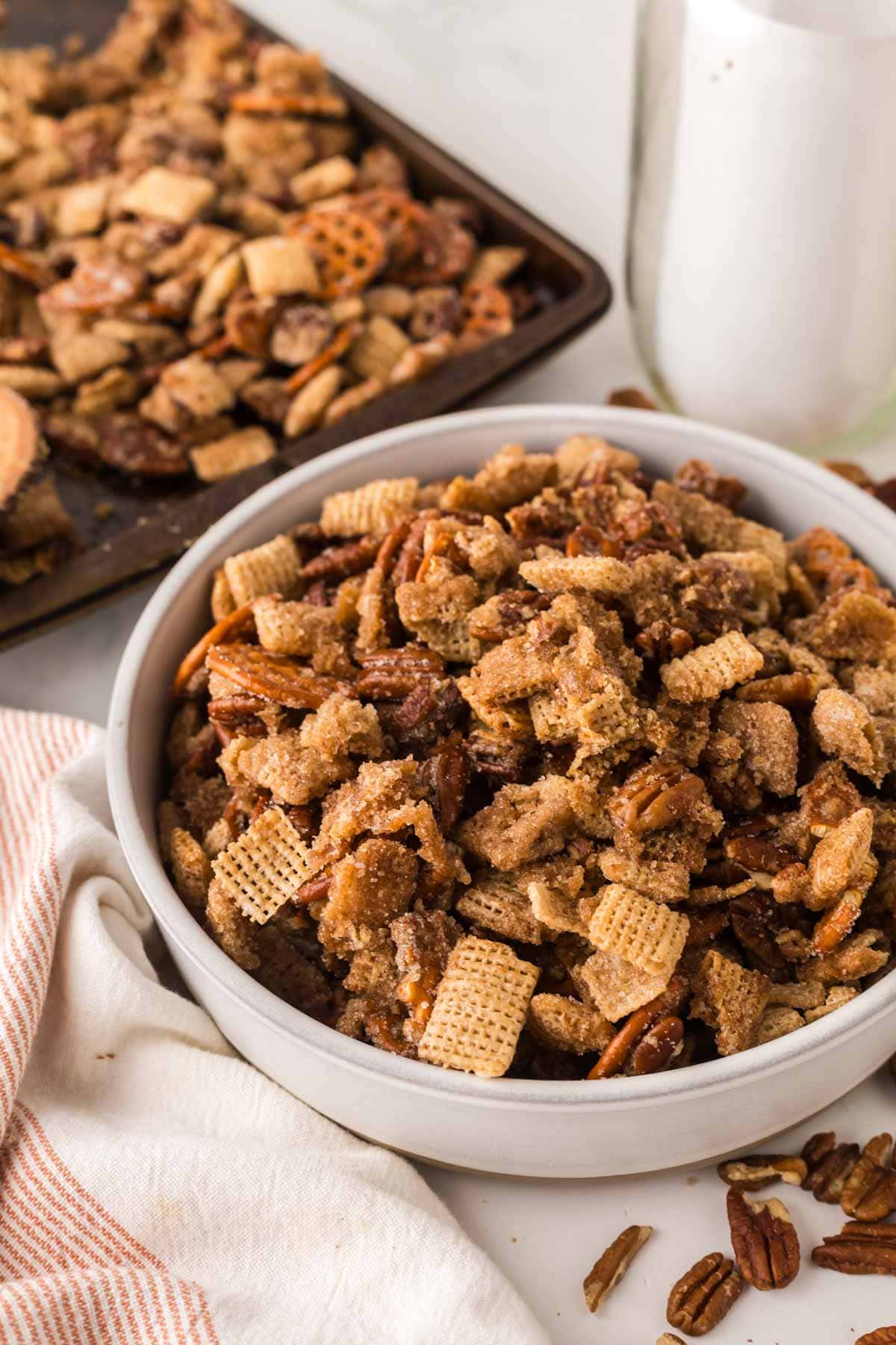 Bowl of praline snack mix next to a glass of milk.