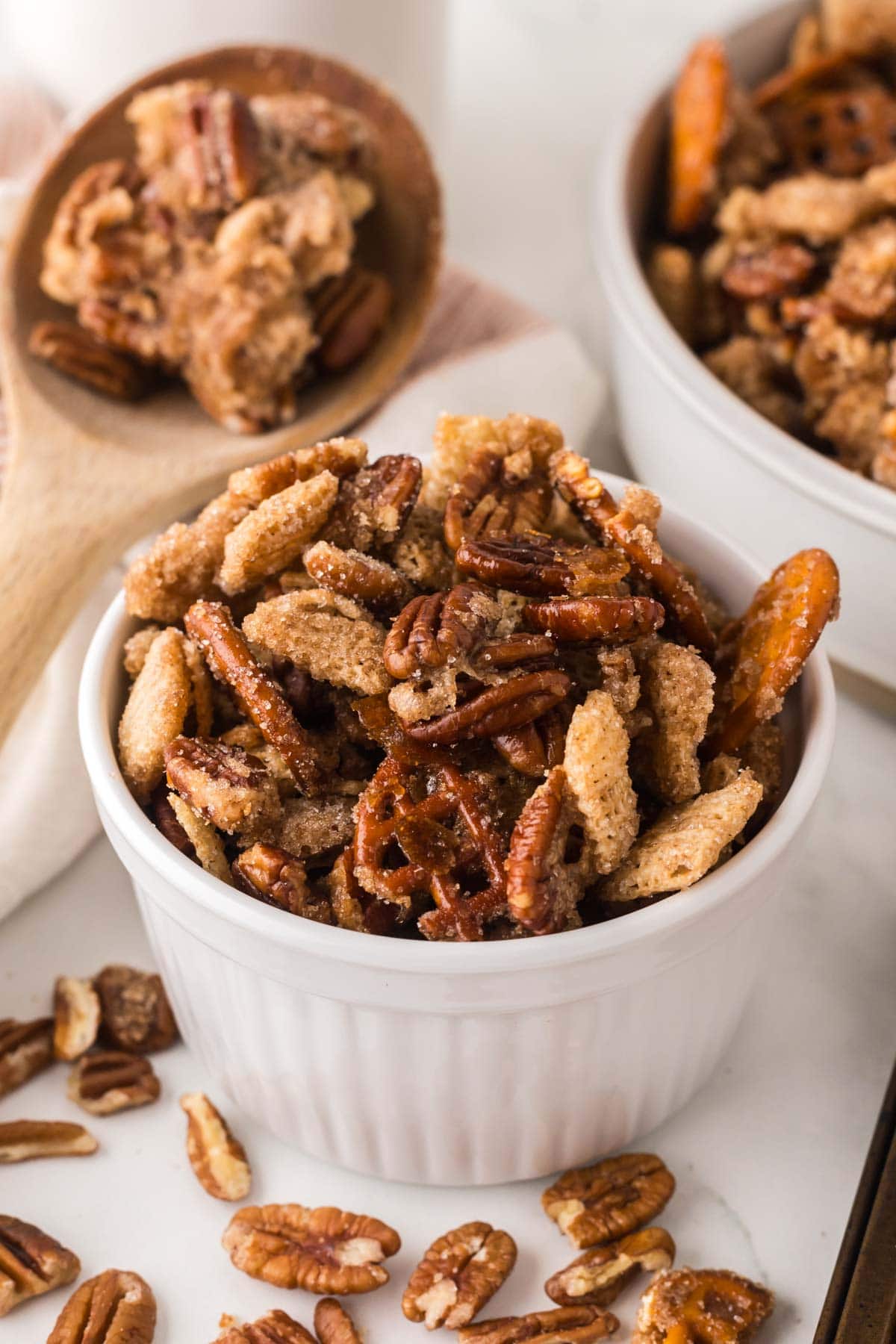 Little bowl of praline snack mix with with pecans around it.