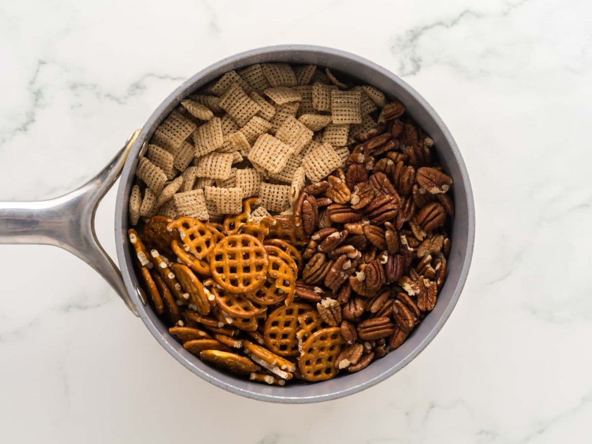 Adding the pretzels, chex and pecans to the melted butter and sugars.