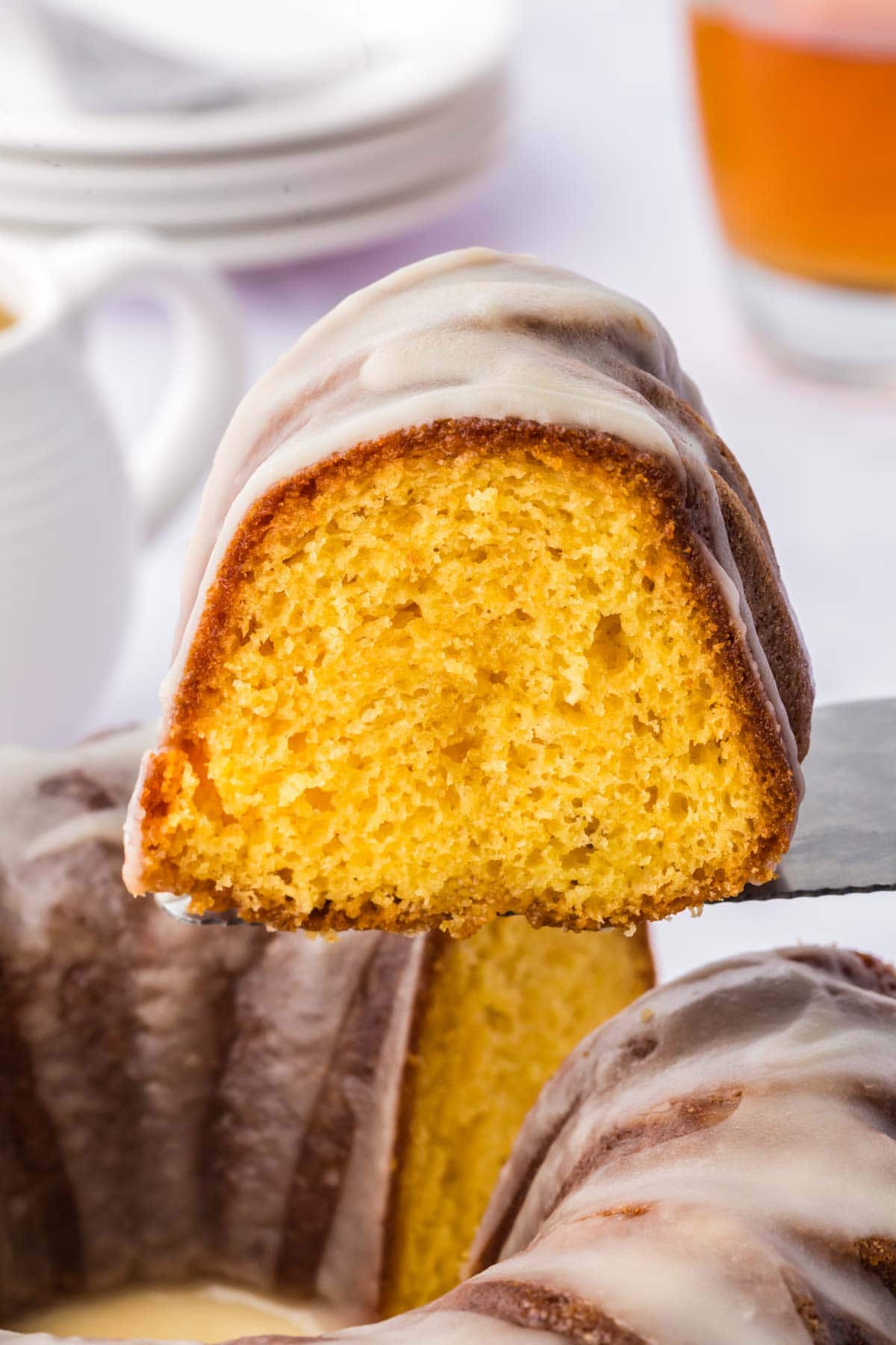 Spatula holding up a piece of the glazed rum cake hovering over the rest of the cake.