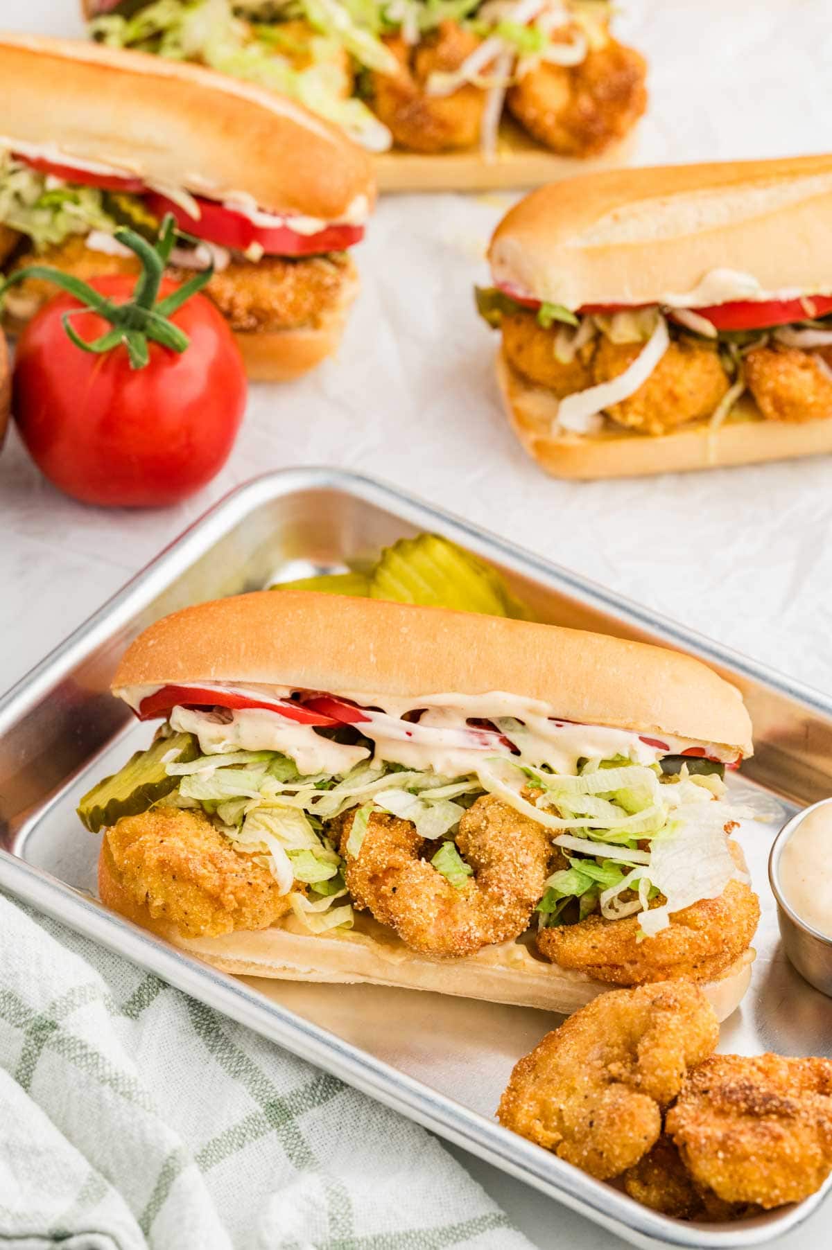 Shrimp po boy on a small sheet pan with more sandwiches in the background.