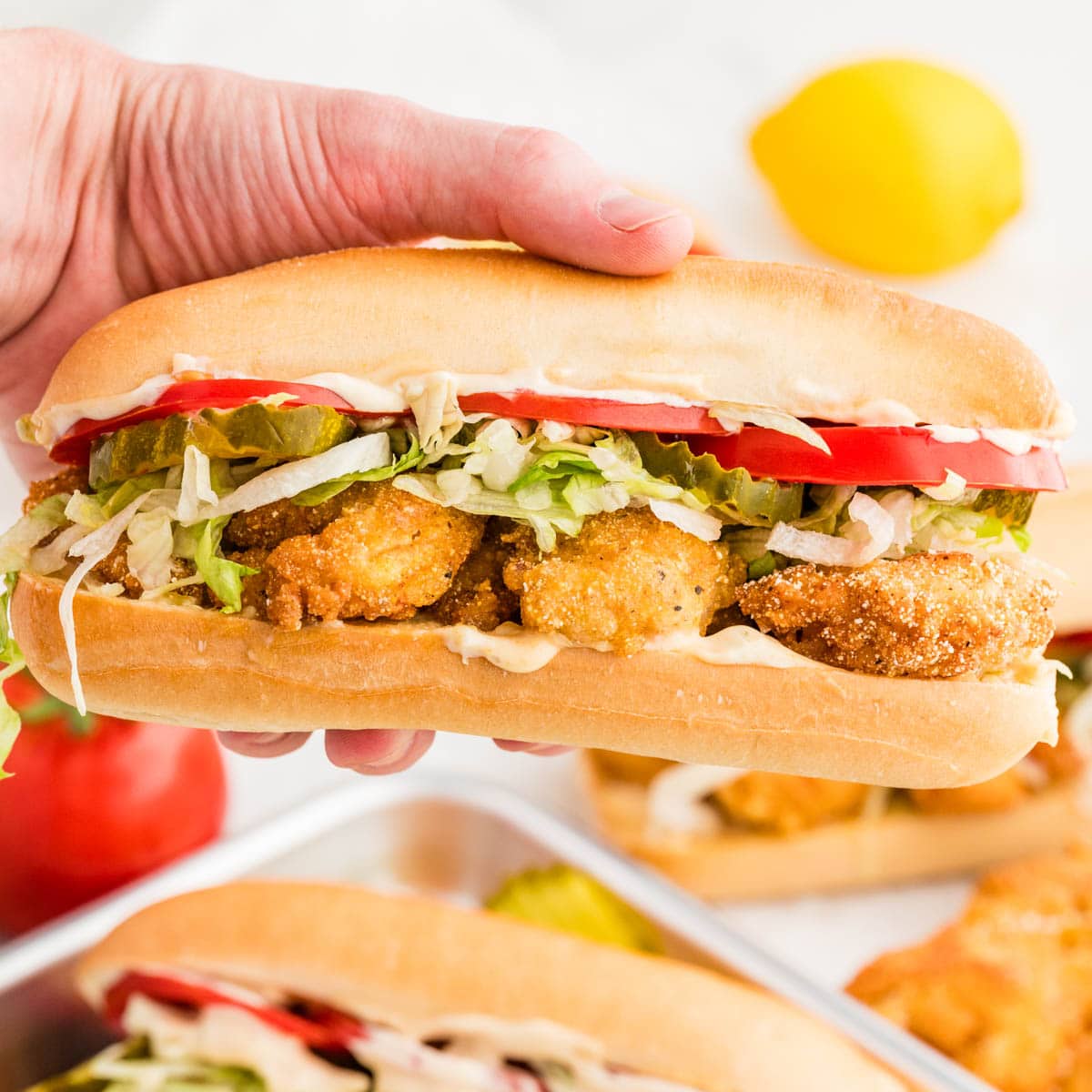 Hand holding the shrimp po boy over a sheet pan of more sandwiches.