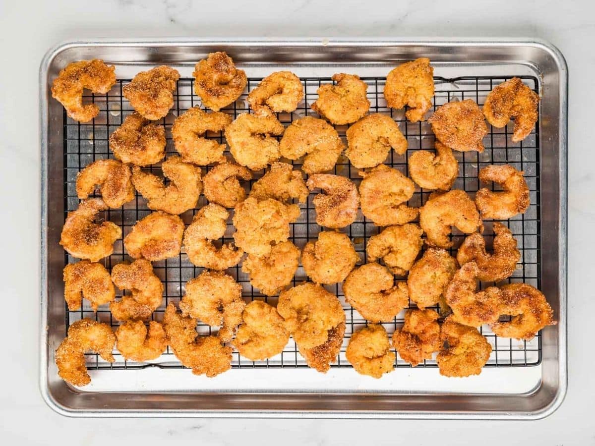 Fried and breaded shrimp on a sheet pan lined with a wire rack.