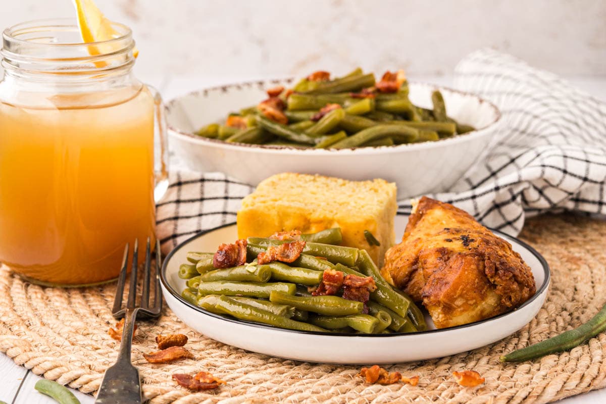 White plate with green beans, fried chicken and corn bread on a southern style table with sweet tea in the background.