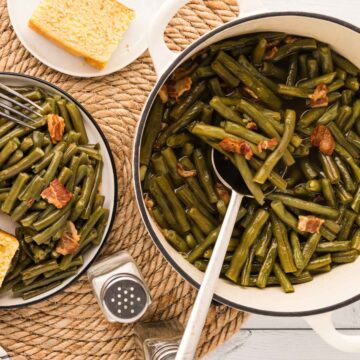 An image of a plate of green beans, side, serving pot of green beans with a silver serving spoon.