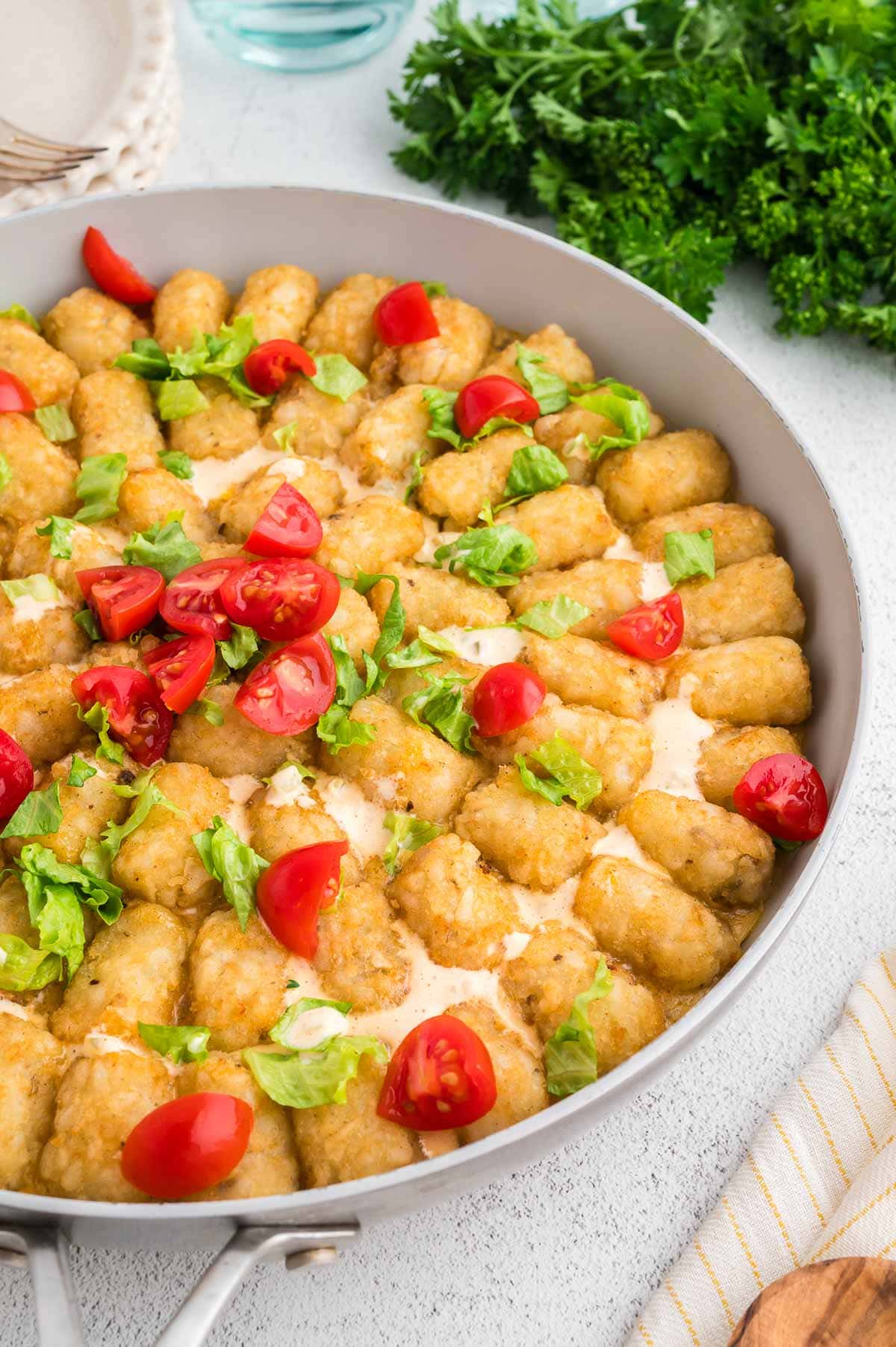 Big mac tater tot casserole in a skillet topped with lettuce and cherry tomatoes.