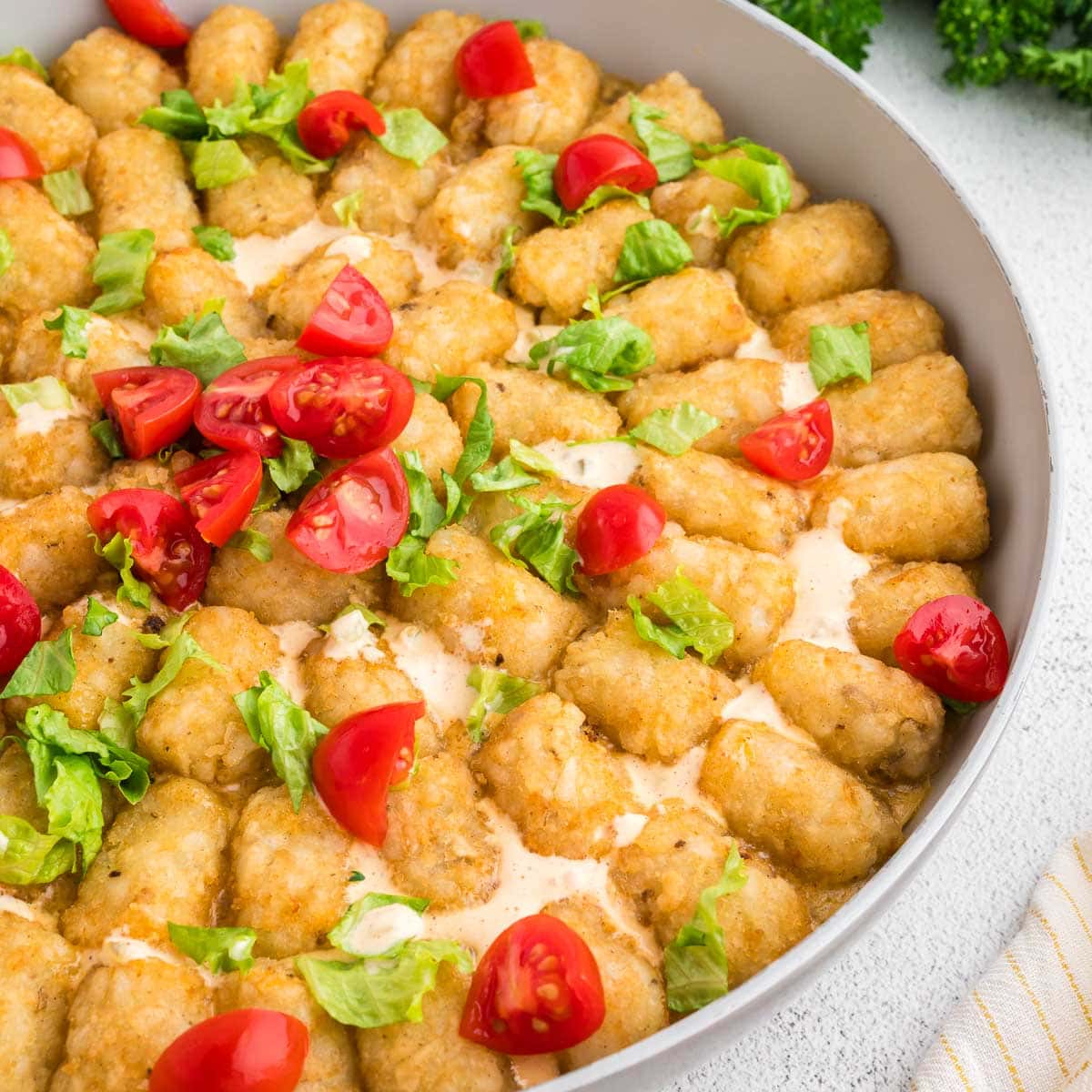 Shot of the big mac tater tot casserole in the skillet garnished with big mac sauce, tomatoes and lettuce.