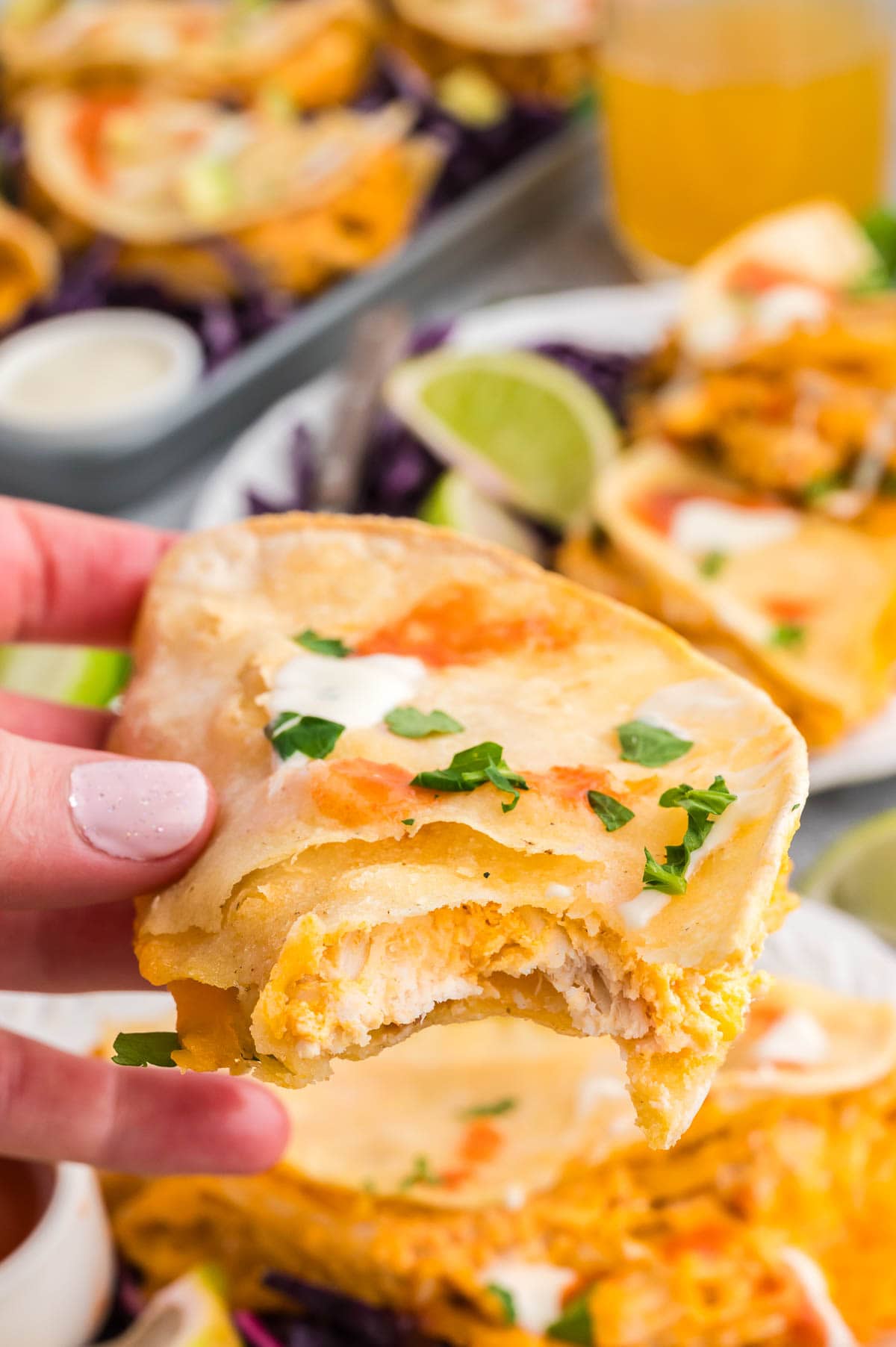 Hand holding a buffalo chicken taco with a bite taken out of it and more tacos in the background.