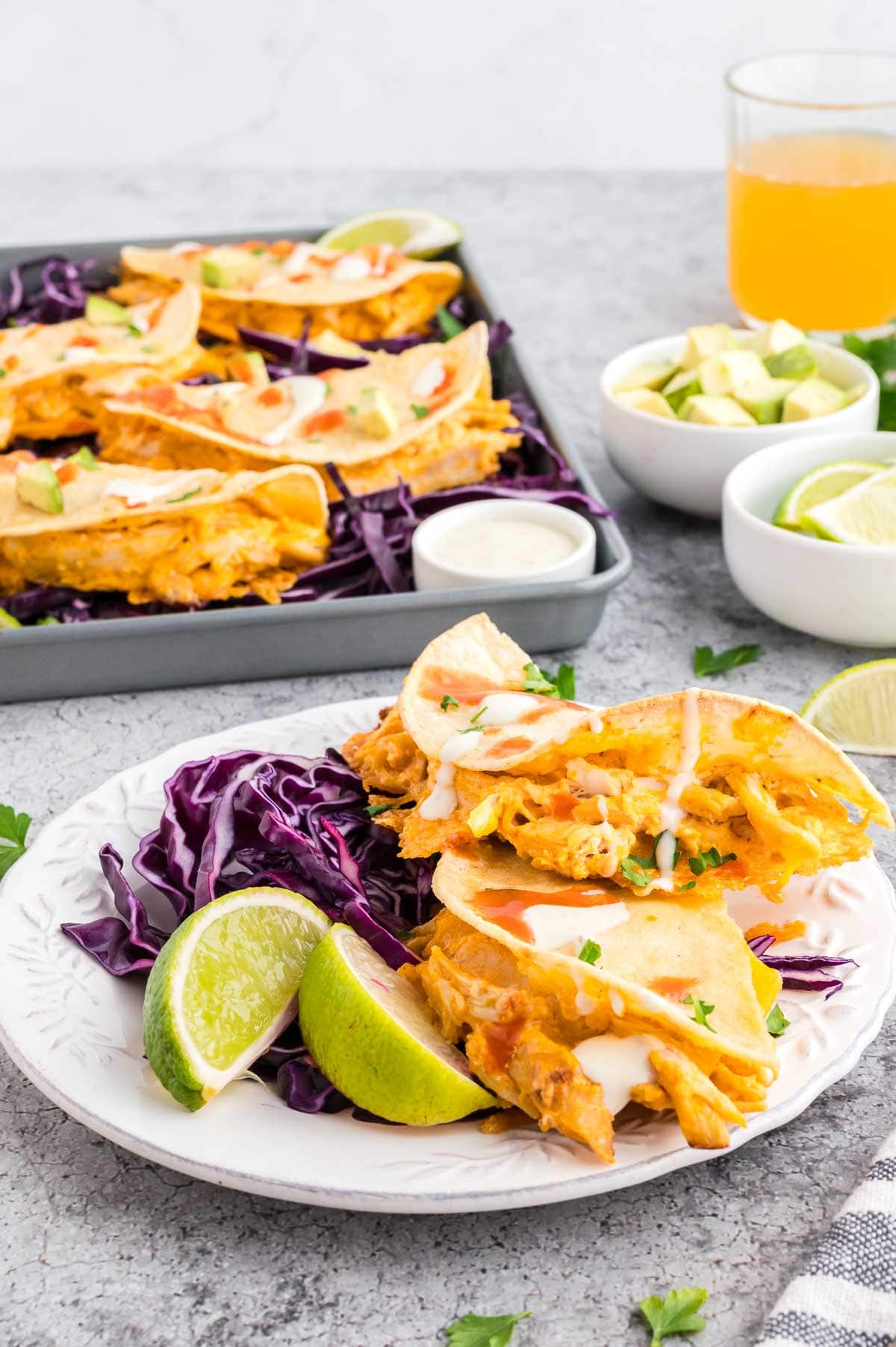 Buffalo chicken tacos on a plate served with red cabbage and lime wedges with more tacos in the background.