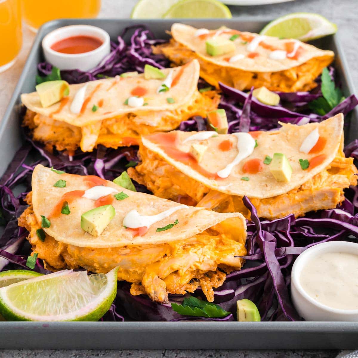 Buffalo chicken tacos served on a bed of red cabbage and topped with drizzles of buffalo sauce and sour cream.