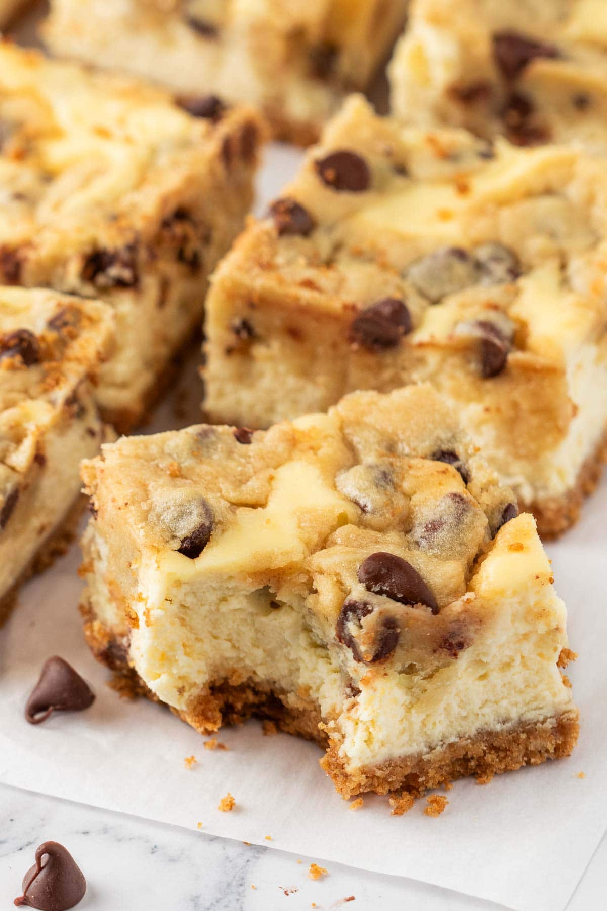 Cookie dough cheesecake bar cut into squares on a parchment paper with one bar missing a bite.