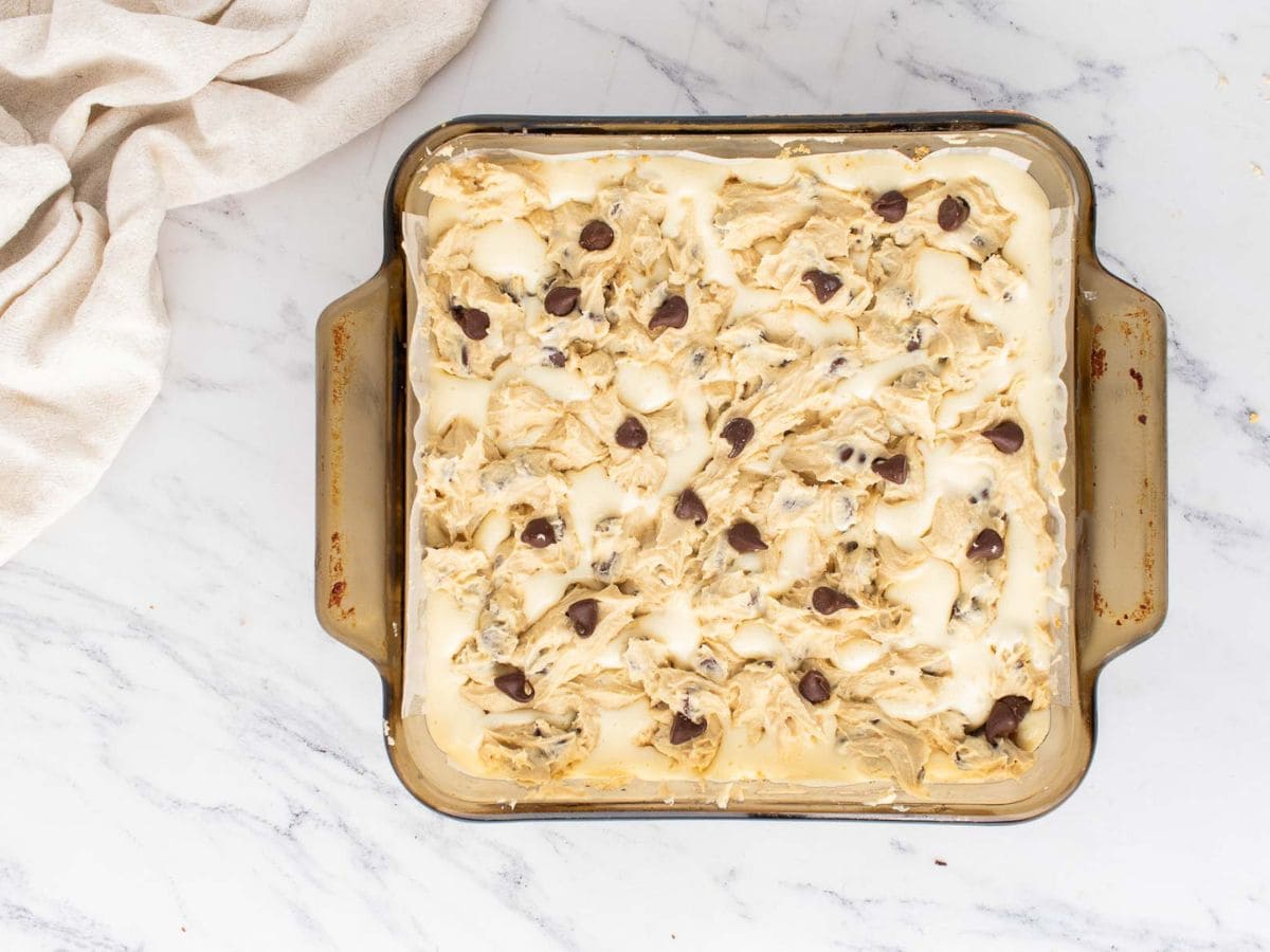 Cookie dough layer added on top of the cheesecake layer in a baking dish.